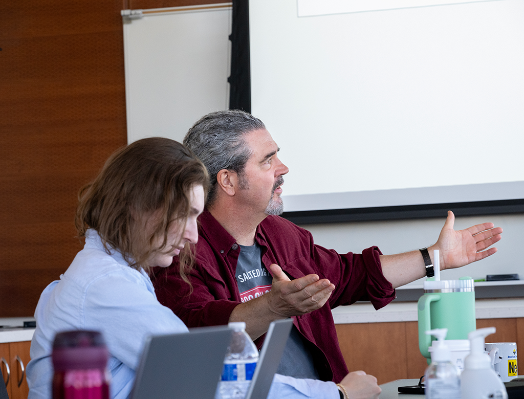Dr. Ed Chapman expressively gestures during lab meeting. Dr. Emma Watson-Roberts listens intently.