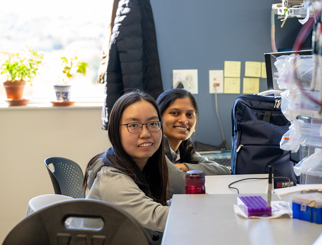 Graduate students Swapnali Patil and Zhaomeng Feng smile for the camera while at their desks.